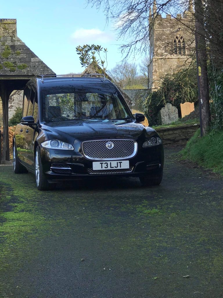 A black hearse arriving at a country churchyard