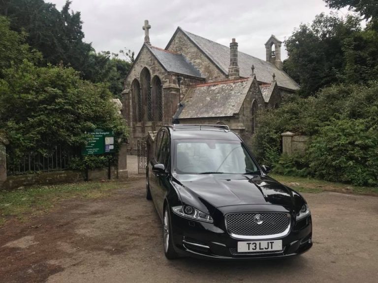 A black hearse outside a stone chapel