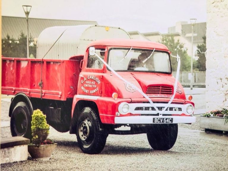 A vintage red lorry decorated with white ribbons for a funeral