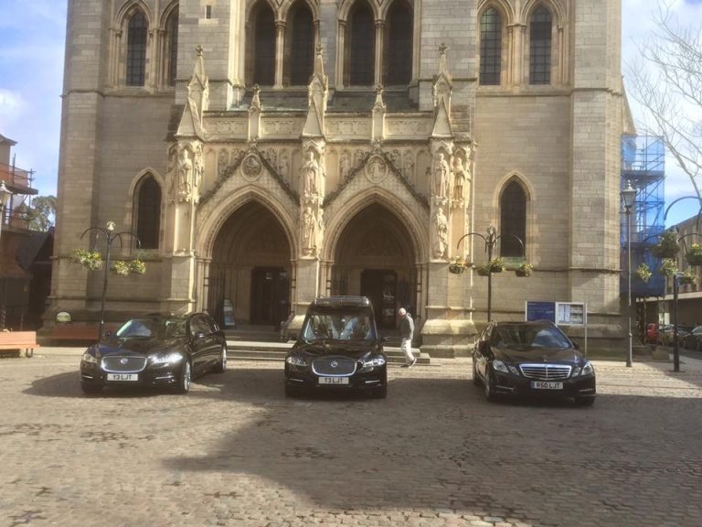 A hearse and family limousines outside Truro Cathedral